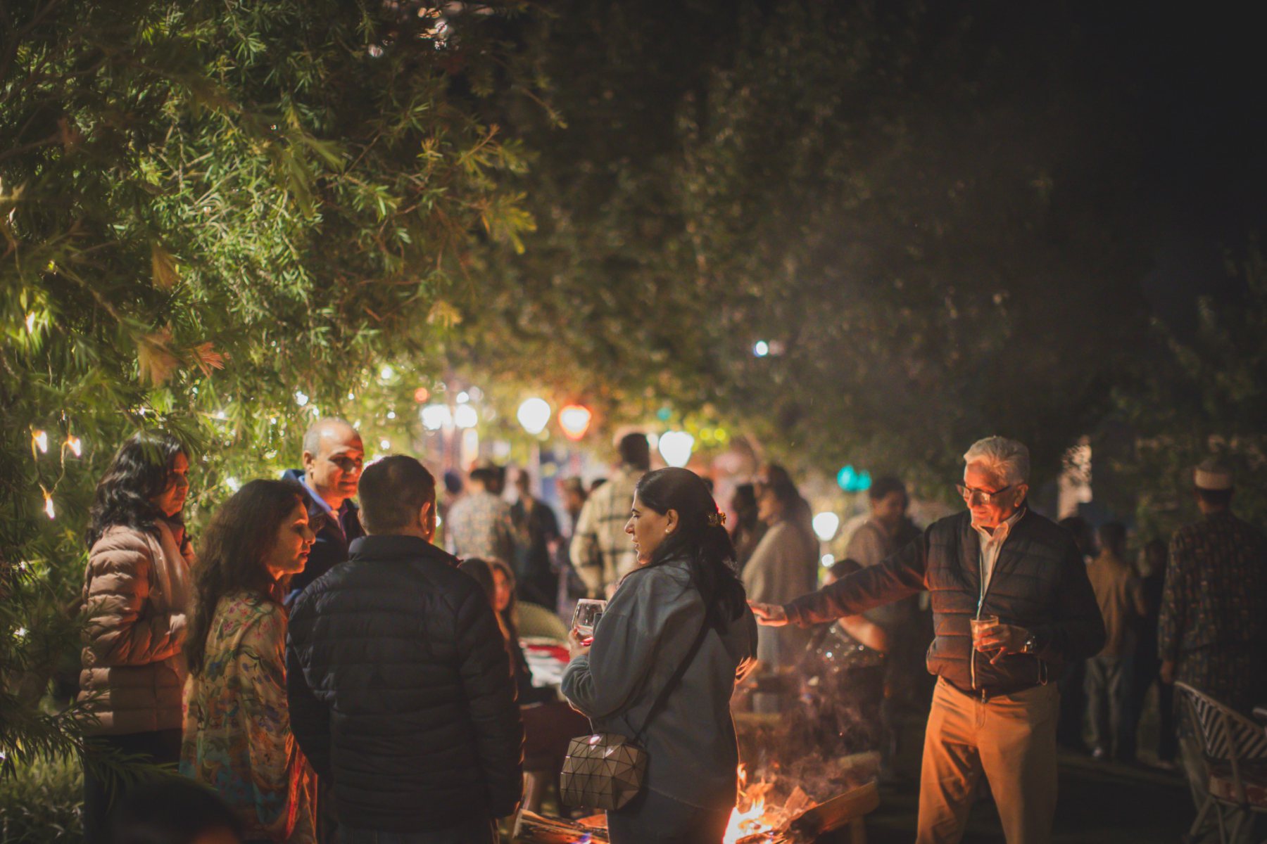 Guests standing and talking around an outdoor fire at the evening festival gathering in Auramah Valley.